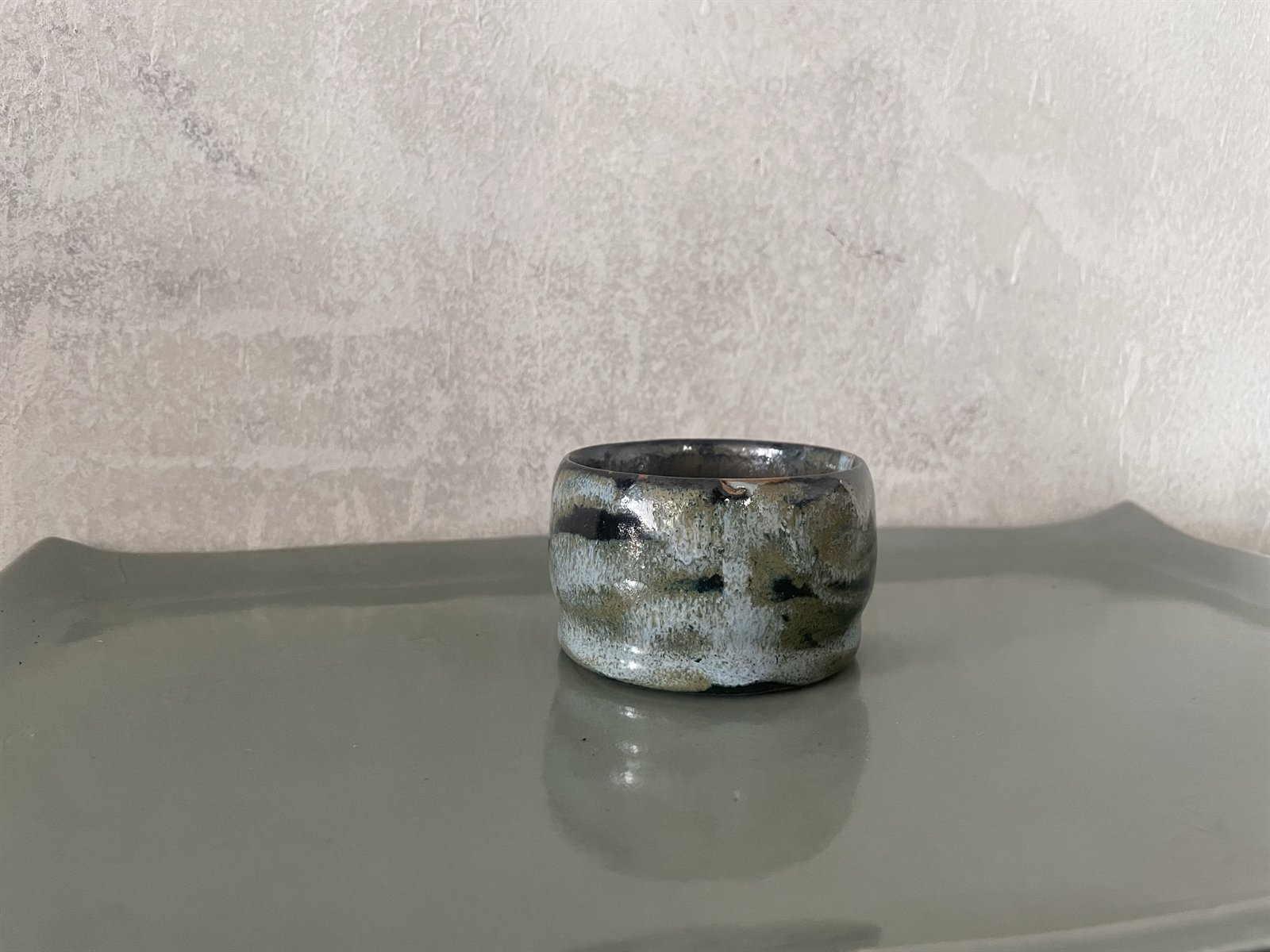 Dark glazed ceramic tea bowl with earthen undertones against natural linen