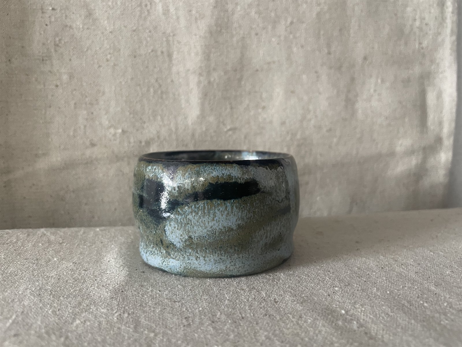 Hand-formed footed ceramic vessel with speckled iron glaze on raw fabric