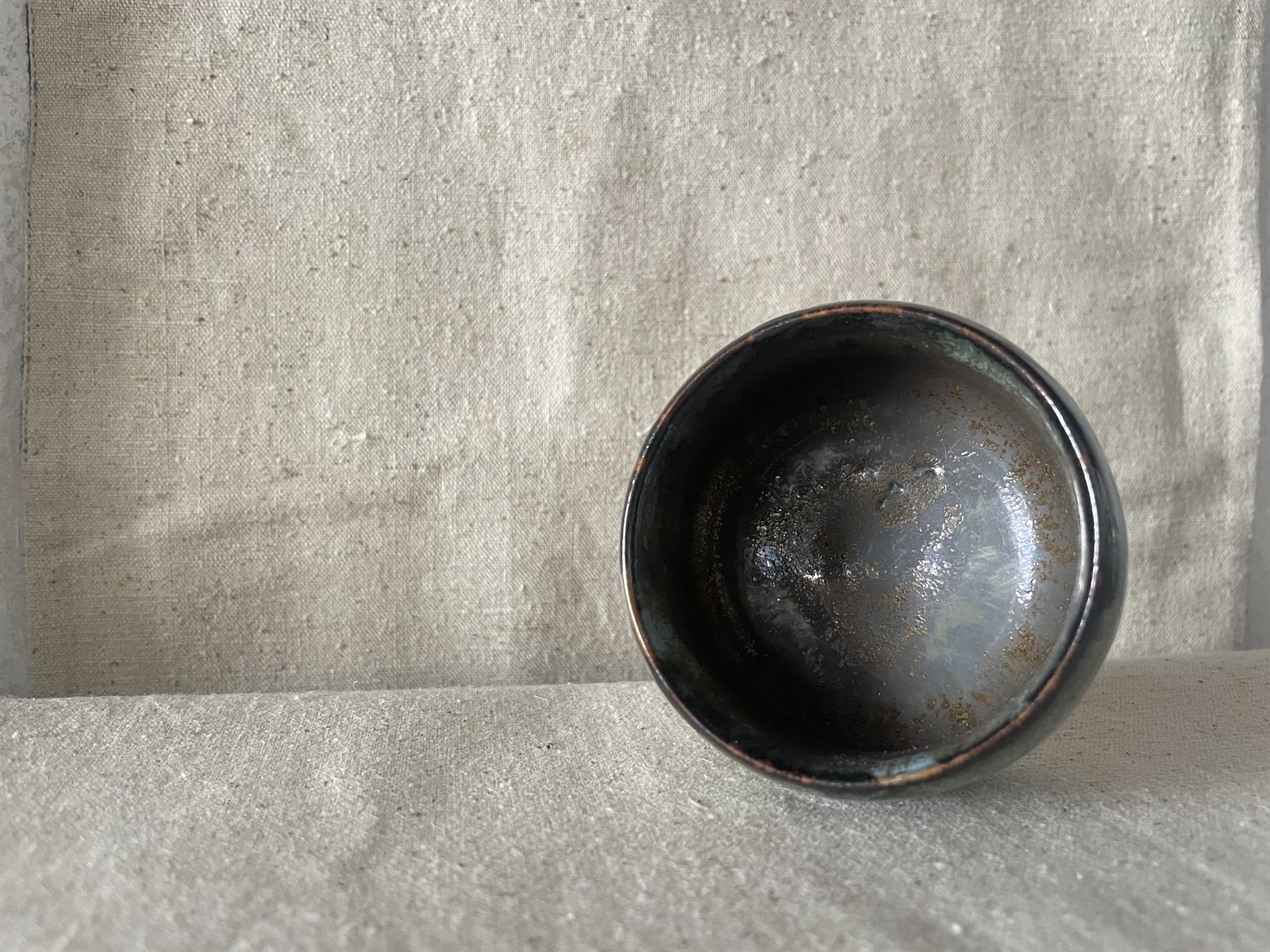 Dark stoneware cup with crystalline pooling rim and metallic patina