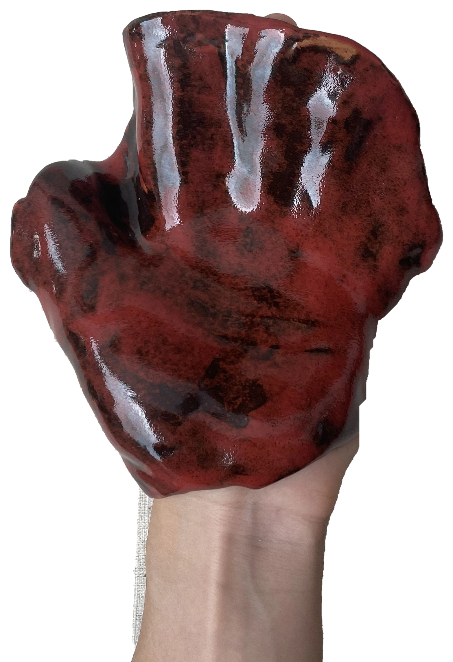 A forearm and hand supporting a glossy red hand-shaped ceramic work