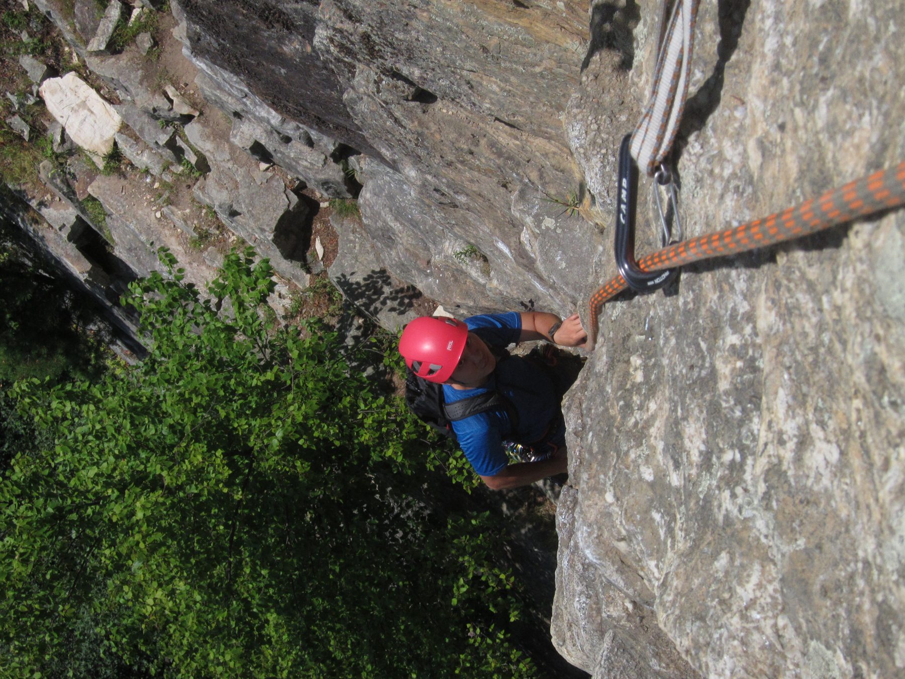 Climber below rock wall looking up along orange rope line